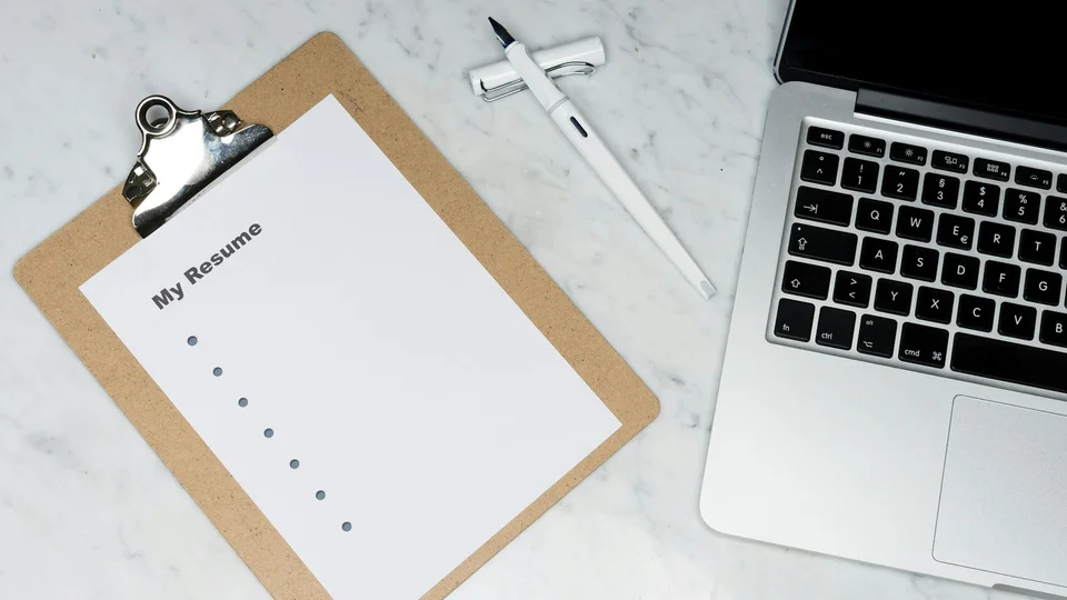 Printed form on a clipboard beside a laptop